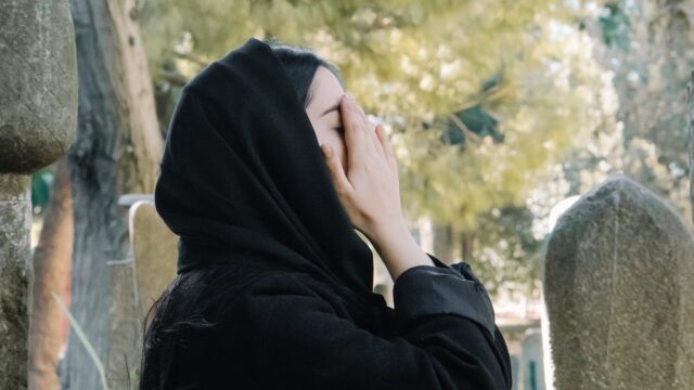 crying woman covering face with hands in cemetery
